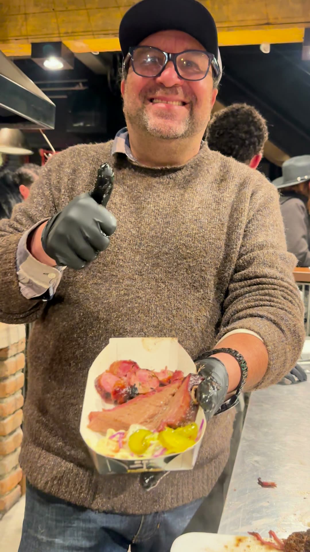 O Dani sorrindo, de boné do BBQ Fronteira, com um prato de brisket na mão